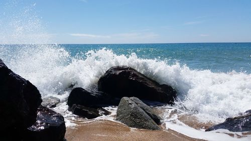 Waves splashing on rocks at wet shore against sky