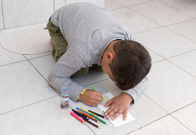 A black-haired boy draws on the floor in his notebook with colored pencils, there are no limits 