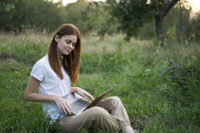 Young woman using mobile phone while sitting on field