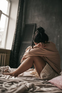 Midsection of woman sitting on bed at home