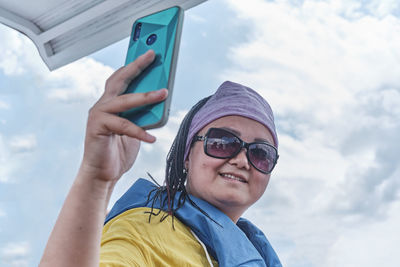 Portrait of smiling man using mobile phone against sky