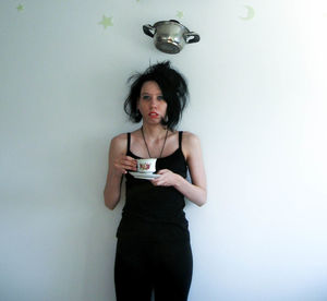 Cooking pan over woman holding cup and saucer against wall at home