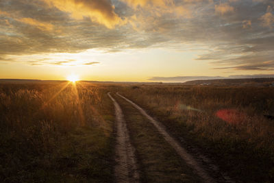 Road amidst field against sky during sunset