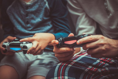 Midsection of father and son playing video game at home