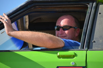 Portrait of man sitting in green car during sunny day