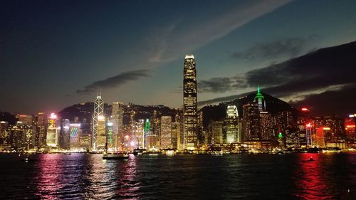 Illuminated buildings by river against sky at night