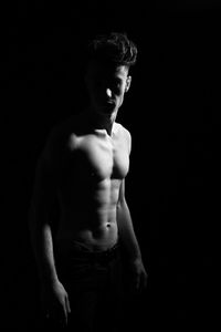 Shirtless young man standing over black background