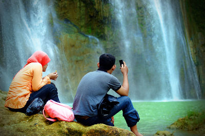 Rear view of people sitting against waterfall