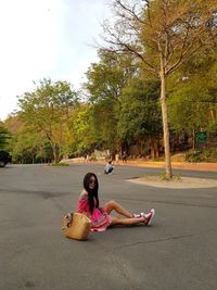 Woman sitting on road against trees