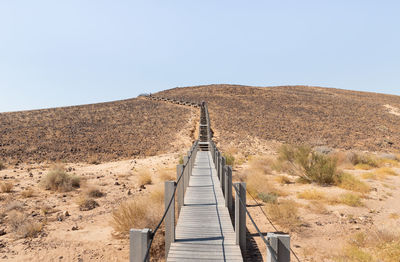 Boardwalk on desert against clear sky