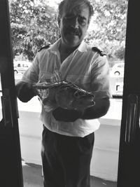 Man holding glass while standing by window