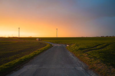 Road amidst field against sky during sunset