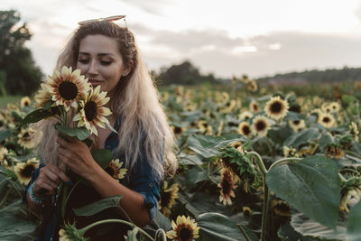 Young woman holding sunflowers while standing at farm