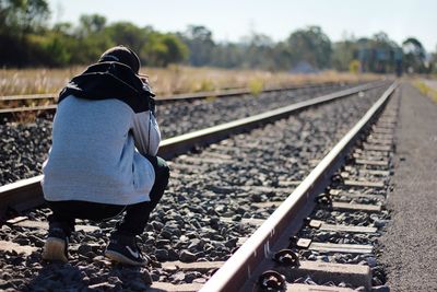 Rear view of man crouching on railroad track 