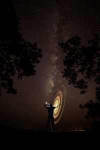 Silhouette person making light painting against sky at night