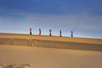 People on sand dune in desert against sky