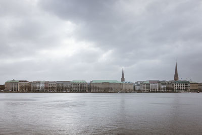 Buildings by river against cloudy sky