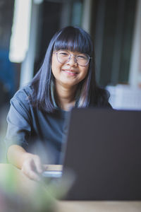 Portrait of a smiling young woman using phone while sitting on table