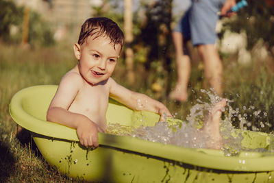 Cute little boy bathing in tub outdoors in garden. happy child is splashing, playing with water