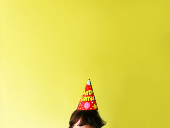 Child wearing party hat against yellow wall