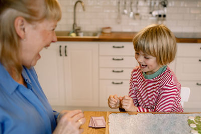 Happy grandson playing board game with grandmother at home