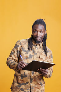 Portrait of young man standing against yellow background