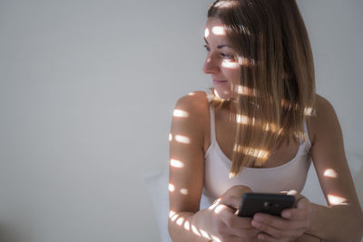 Smiling woman using mobile phone while relaxing on bed at home