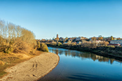 Scenic view of river by buildings against clear blue sky