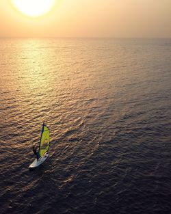 Man surfing in sea against sky during sunset