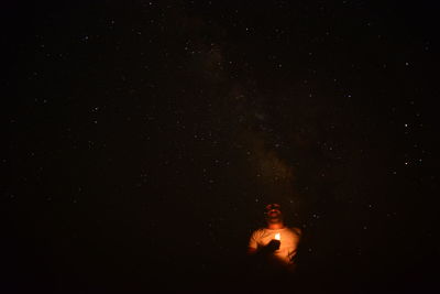 Man holding illuminated candle against sky at night