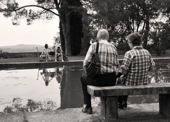 Rear view of people sitting on lake against trees