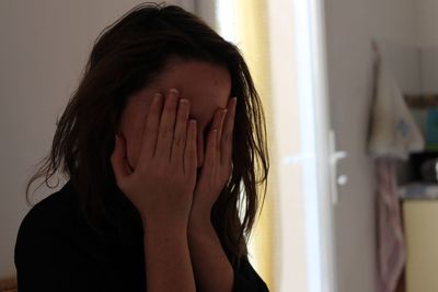 Portrait of woman covering face at home