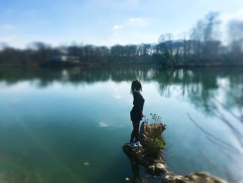 Man standing on rock by lake against sky