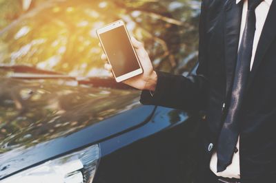 Midsection of man holding smart phone by car