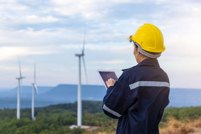 Rear view of engineer examining windmill through digital tablet