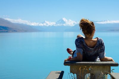 Rear view of woman sitting by sea against sky