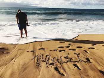 Rear view of man standing on shore at beach during sunny day