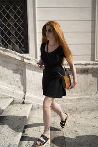 Red hair girl walking up the stairs holding a phone in sunny day