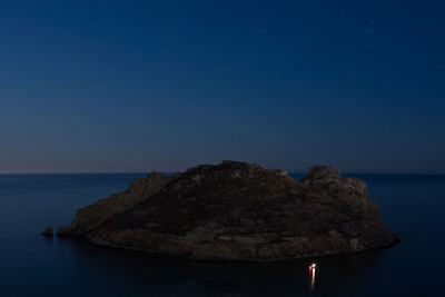 Rocks by sea against clear blue sky at night