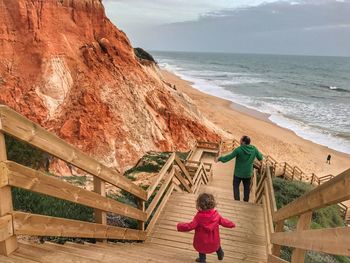 Rear view of father and daughter moving down on wooden steps at beach