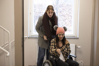 Female caregiver helping woman sitting on wheelchair at home