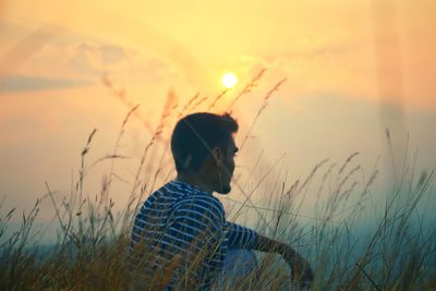 Side view of man sitting on field against sky during sunset