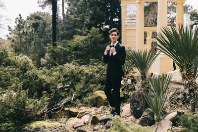 A beautiful young man, the groom in an elegant wedding suit, stands posing in the city's old park