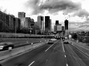 Vehicles on road by buildings in city against sky