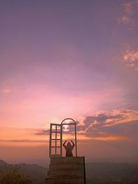 Rear view of woman sitting against dramatic sky during sunset