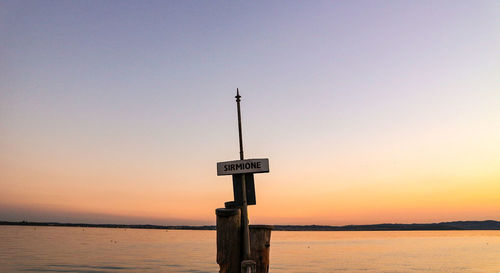 Information sign on wooden post in sea against clear sky