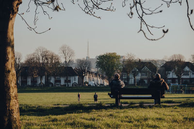 People standing on field by trees against sky