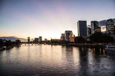 Buildings by river against sky during sunset