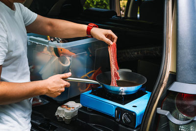 Midsection of man preparing food on camping stove in car trunk