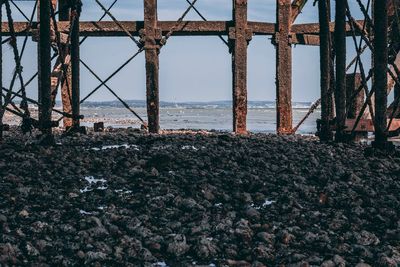 Rusty metallic structure on beach against sky